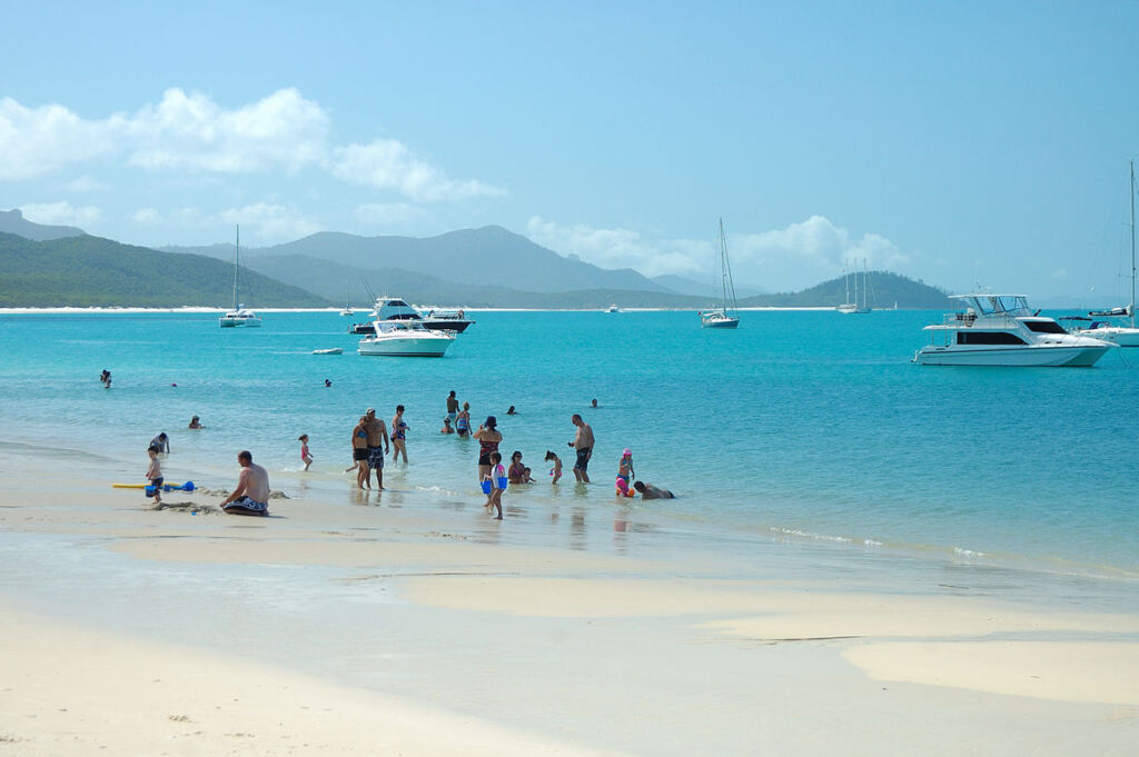 Photo showing Whitehaven Beach with people enjoying the white sand and calm water on on of the most stunning beaches in the world