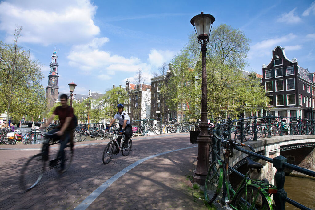 Photo showing bikers crossing a bridge in Amsterdam with Westerkerk in the background, one of the epic cycling routes in the city