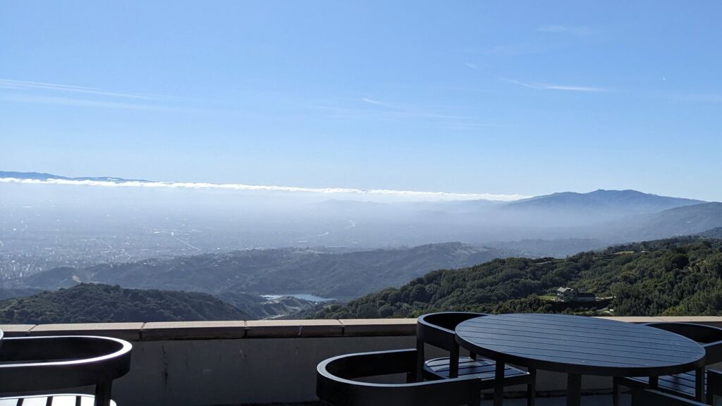 Round tables on a patio overlook a foggy valley below.
