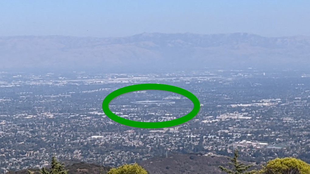 The circular Apple headquarters seen from the mountains on a hazy day.